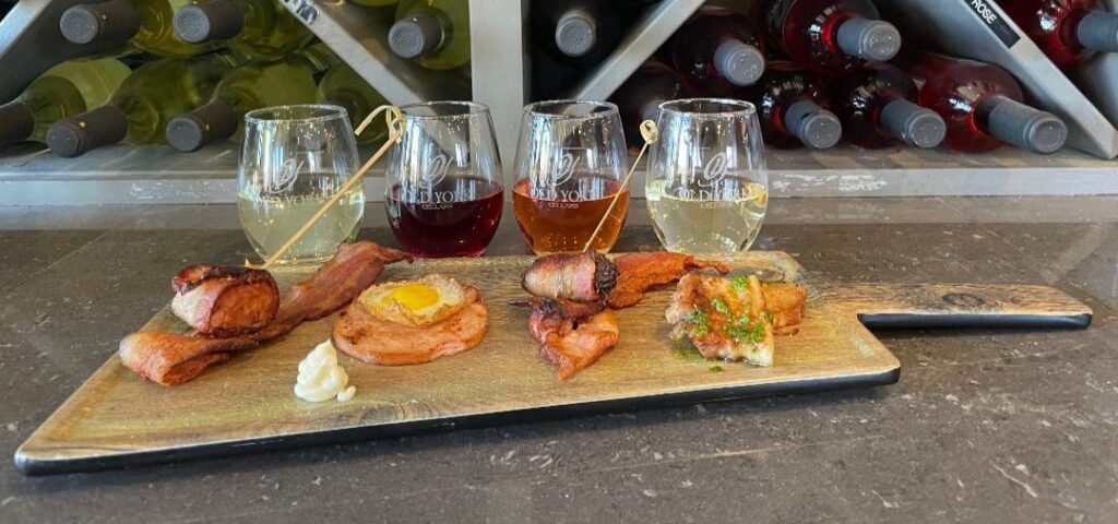 Wine & Bacon Pairing wooden board with wine glasses and small plated appetizers arranged for a tasting experience.