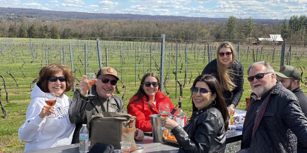 Guests sipping wine at Old York Cellars vineyard with scenic views and sunshine