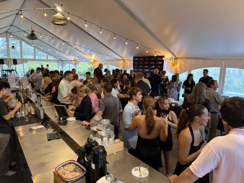 Guests socializing and enjoying wine and food under the Old York Cellars event tent with vineyard views and a lively atmosphere.