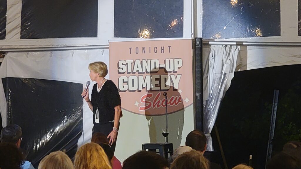 Comedian Helene Angley performing a stand‑up show at Old York Cellars with a “Tonight Stand‑Up Comedy” sign behind her and guests seated in the audience.