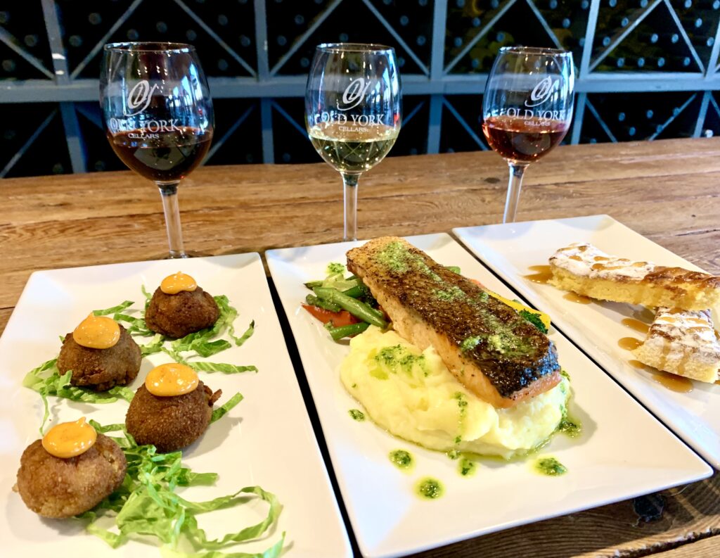 Gourmet wine pairing featuring seared scallops and a fish entrée on white plates, served with three glasses of red wine on a wood table in Old York Cellars Vista Room located in Hunterdon County NJ