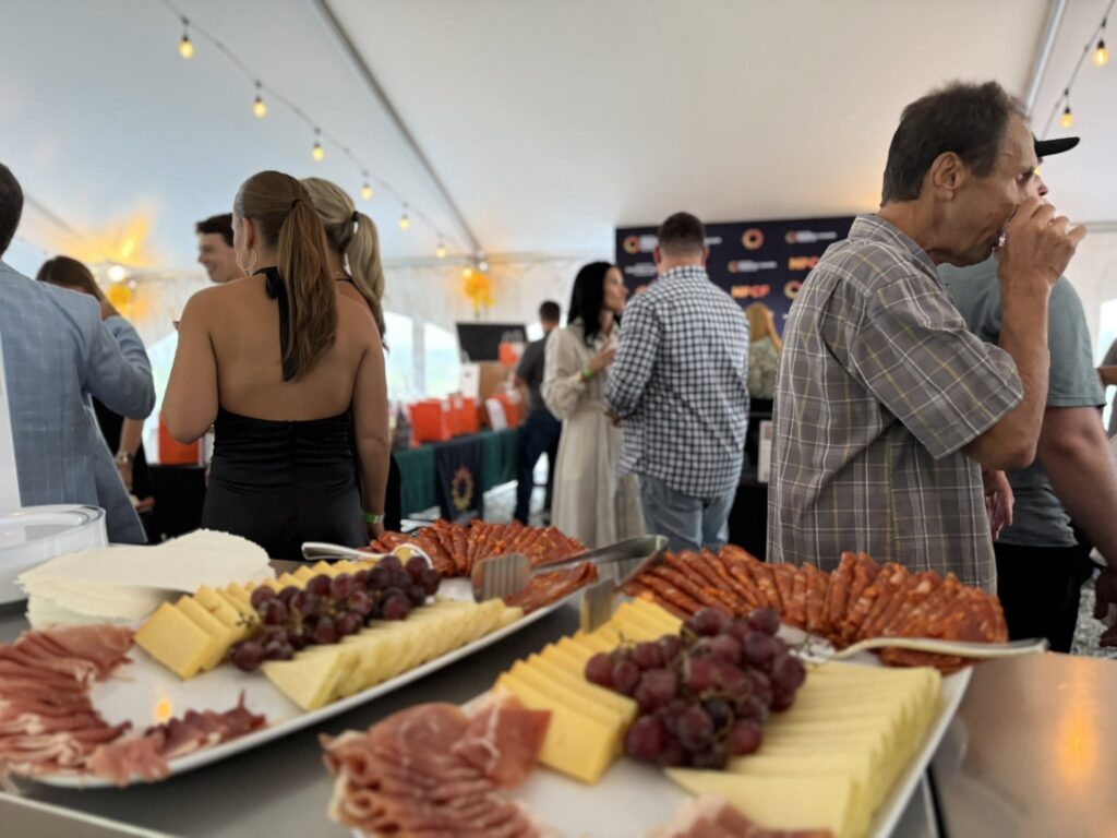 Guests mingling under the vineyard tent at Old York Cellars in Ringoes, Central NJ, beside a catering table with assorted cheeses and charcuterie prepared by Chef José Diaz.