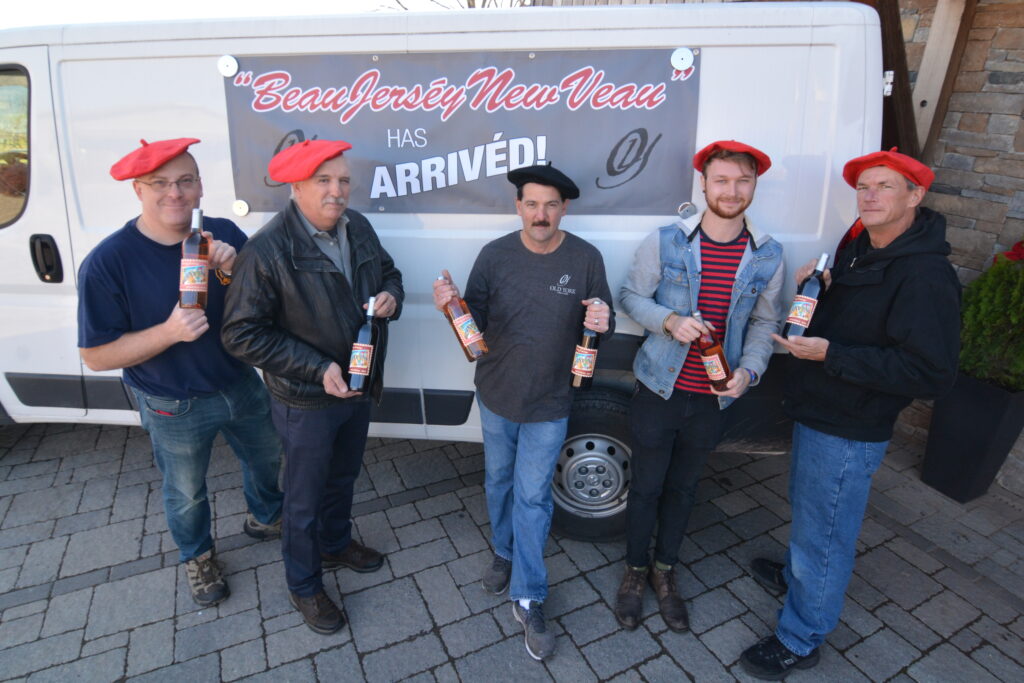 Old York Cellars' Winemakers wearing red berets holding bottles of wine in front of a trailer with a banner reading “Beau Jersy New Veau Has Arrived