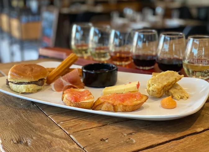 Brunch tasting plate at Old York Cellars featuring a slider, cured meats, cheese, and small bites paired with a flight of wines on a wood table.