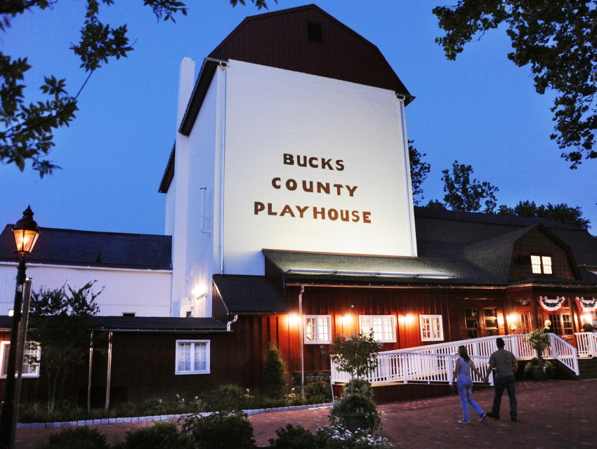 Exterior of Bucks County Playhouse at dusk with warm lights and visitors walking near the entrance.