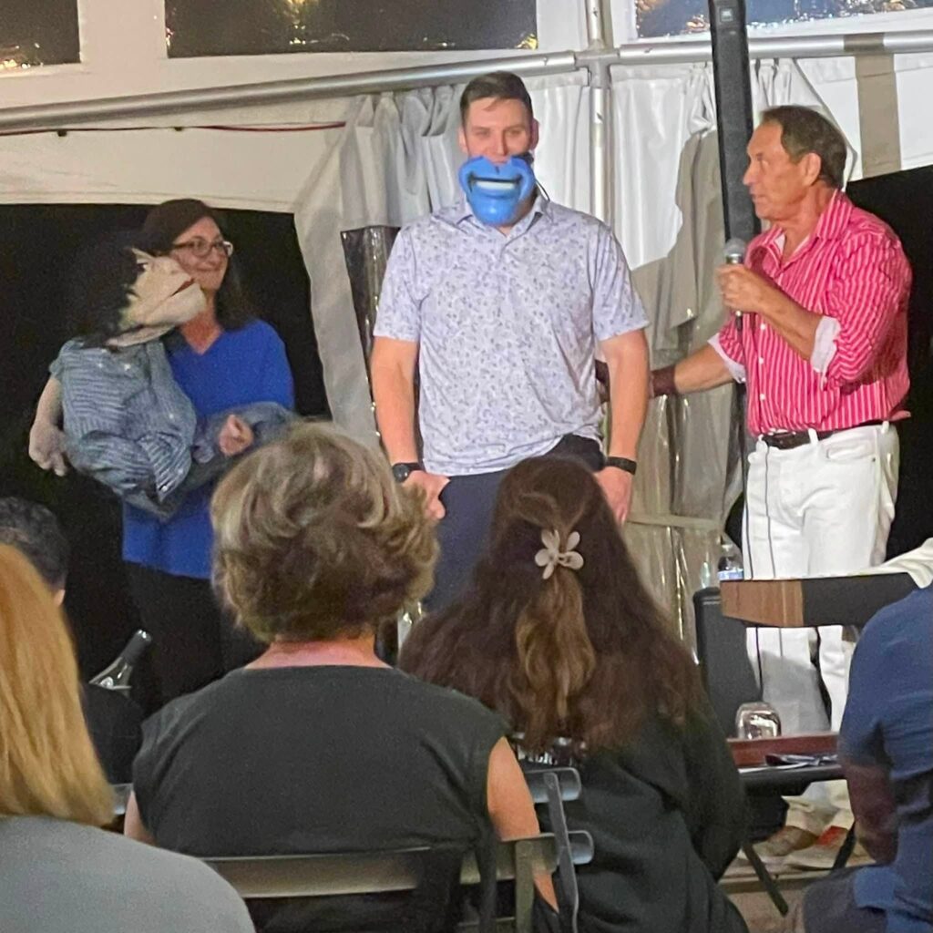 Comedian Taylor Mason performing under the vineyard tent at night with a spotlight casting a shadow on the backdrop.