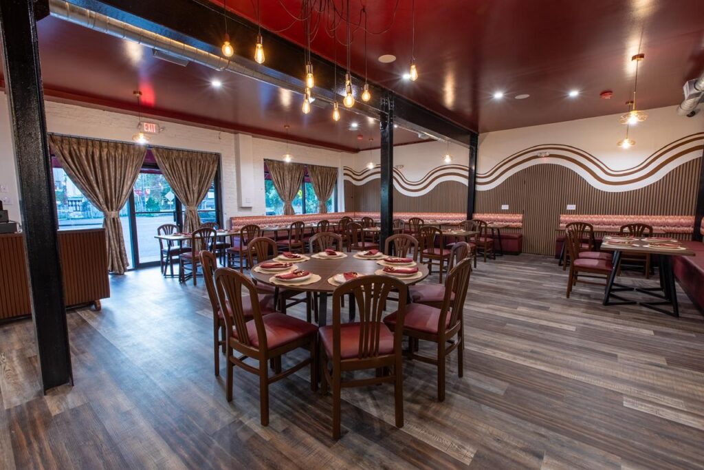 Dining room interior with wooden tables and chairs, warm lighting, and decorative wall patterns at Eight Indian Bistro.