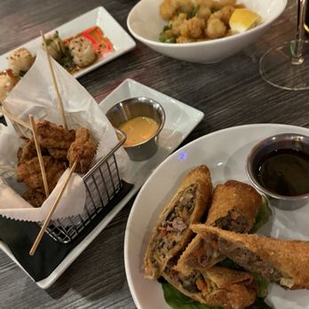 Close‑up of plated appetizers including spring rolls, fried bites, and dipping sauces on a dark tabletop at AARZU Modern Bistro in Freehold, NJ.