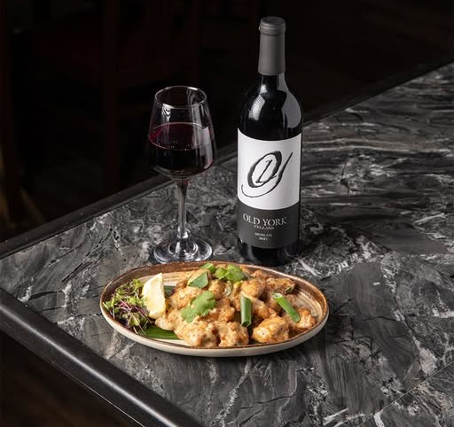 Plate of Indian food with a glass and bottle of Old York Cellars red wine on a dark marble table at Eight Indian Bistro in Edison, NJ.