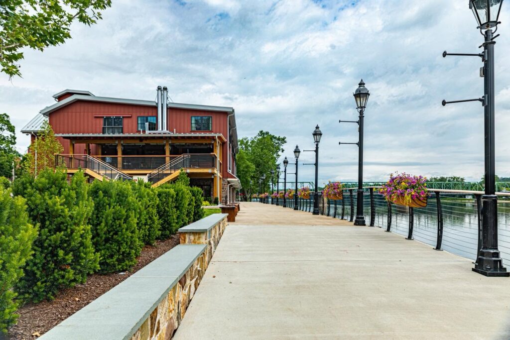 View of the riverwalk outside Ghost Light Inn, showing a paved path lined with streetlamps and greenery leading toward the Delaware River.
