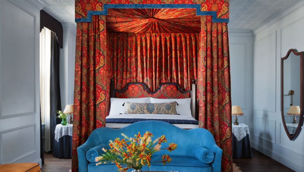Guest room at Graduate by Hilton Princeton with a canopy bed draped in red and blue fabric, a blue bedspread, and a vase of yellow flowers at the foot of the bed.