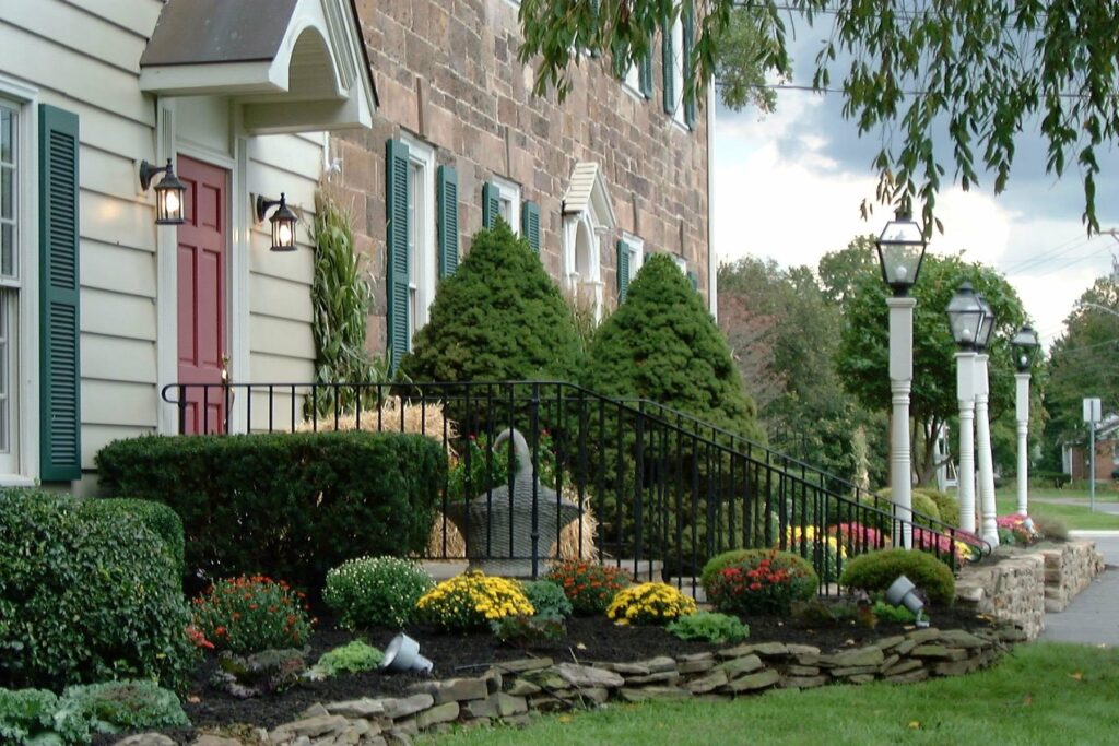 Landscaped entrance with evergreens and flowers leading to the stone façade of Harvest Moon Inn.