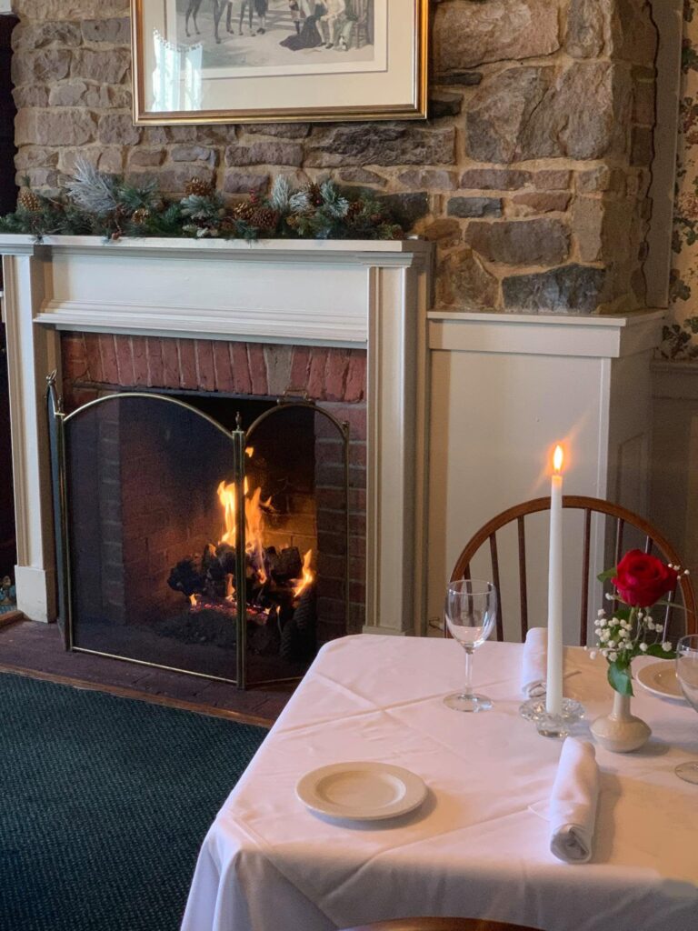 Elegant table set with candles beside a lit stone fireplace inside Harvest Moon Inn.