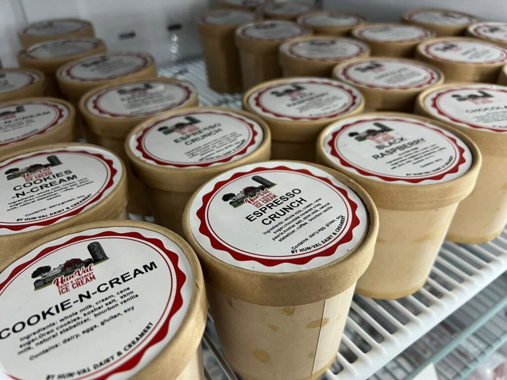 Pints of Hun‑Val Dairy homemade ice cream labeled ‘Chocolate Cheesecake’ in a refrigerator case