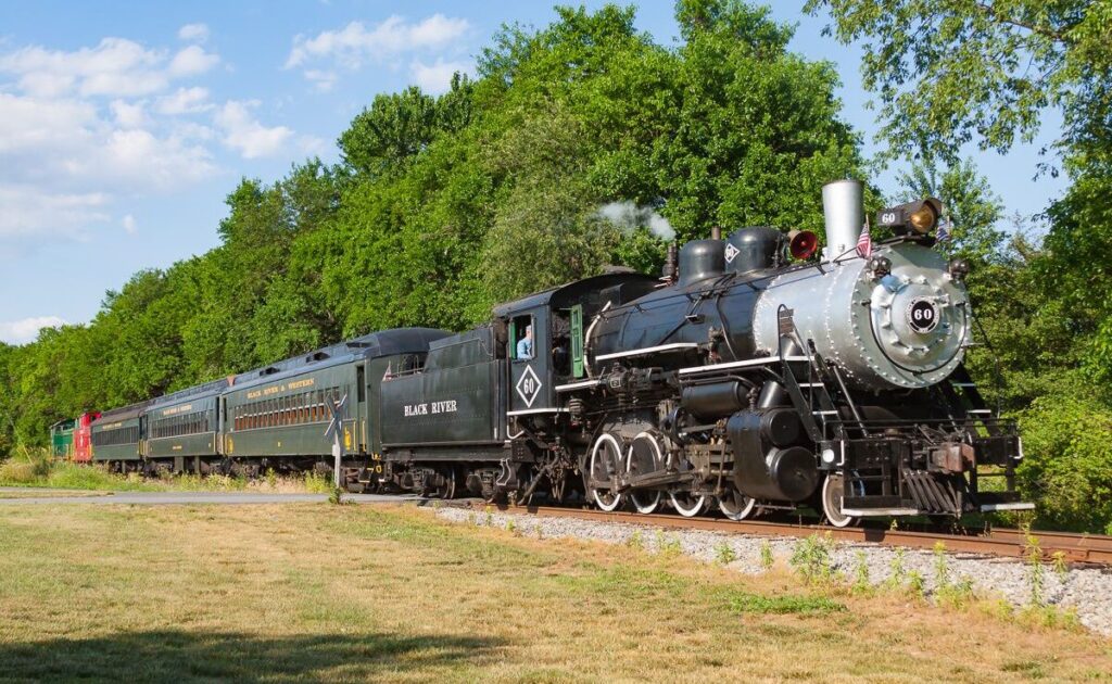 Historic Black River & Western Railroad steam locomotive traveling through green farmland under a blue sky.