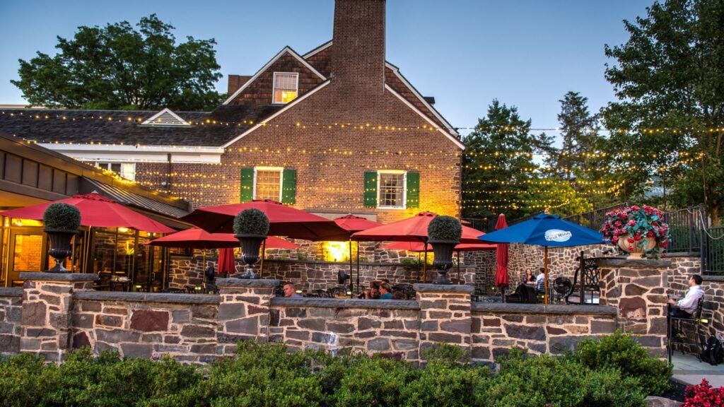 Outdoor dining area at Nassau Inn featuring stone walls, colorful umbrellas, and patio seating beside the historic building and chimney.