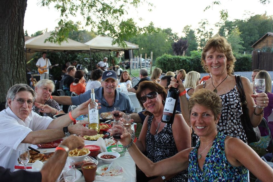 Large group of guests celebrating at Old York Cellars in Ringoes, NJ, raising wine glasses and bottles during an outdoor dining event.