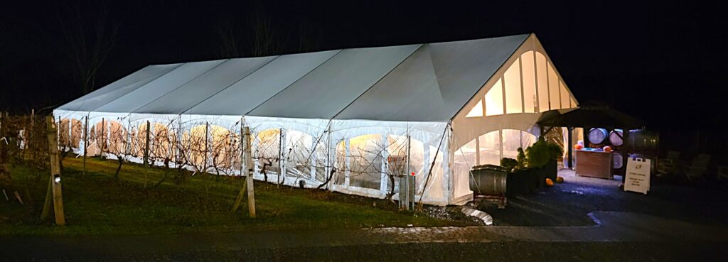 Large white vineyard tent at Old York Cellars illuminated at night, glowing warmly against the dark sky.