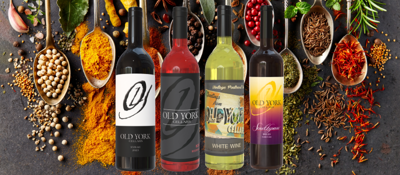 Four Old York Cellars wine bottles displayed against a backdrop of vibrant spices and herbs including turmeric, chili, and coriander.