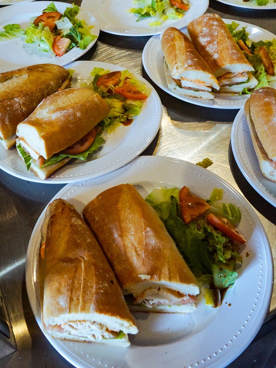 Plated sandwiches made with crusty baguette bread, filled with lettuce, tomato, and sliced chicken, served with a small side salad of greens and tomatoes.