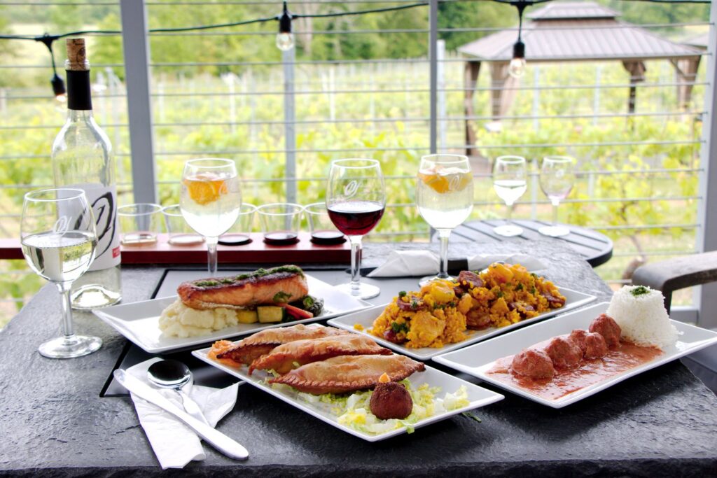 Elegant wine and food tasting setup overlooking Old York Cellars central NJ vineyard, with assorted dishes, cured meats, and multiple glasses of white and red wine.
