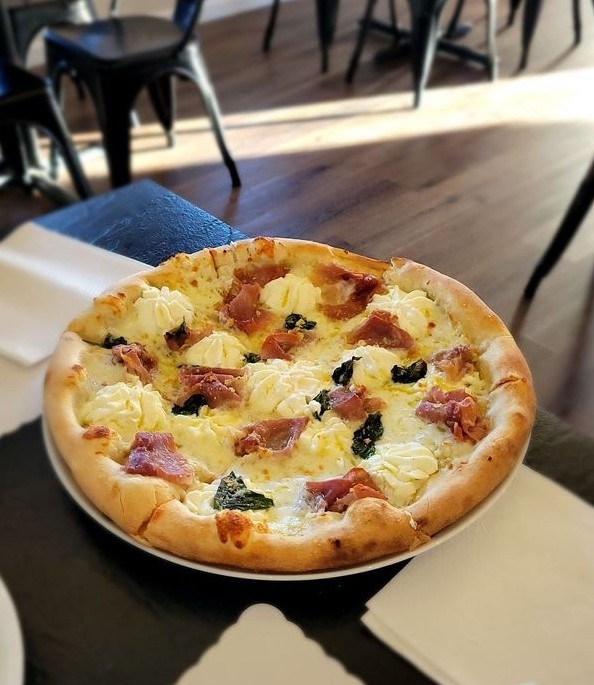 A golden‑crusted pizza topped with melted cheese, herbs, and savory toppings, served on a wooden table at the cozy Luna Pizza Restaurant in Three Bridges, New Jersey restaurant offering Old York Cellars wines.
