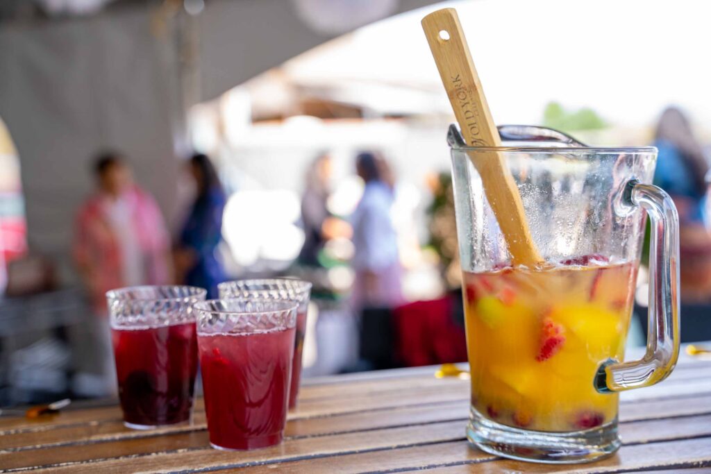 Pitcher of sangria with fruit and two glasses on a wood table at Old York Cellars, with guests socializing.