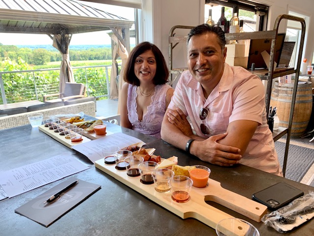Guests enjoying a food and wine pairing experience at Old York Cellars Winery in Ringoes, Hunterdon County, NJ, seated indoors beside a long tasting board filled with assorted sauces and dips, with vineyard views in the background.