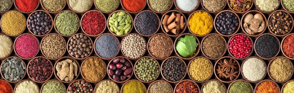 Overhead view of assorted colorful spices and herbs arranged in small round containers, showcasing the variety of Indian seasonings.