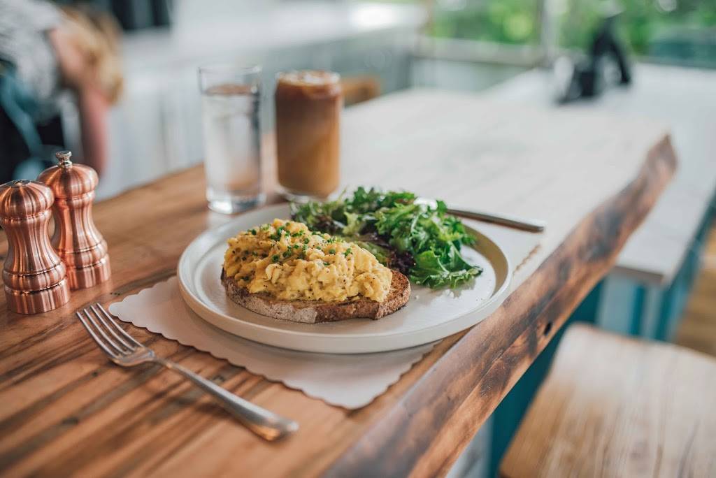 A plate of scrambled eggs on toast with a side of greens, accompanied by iced coffee and water, highlighting a brunch pairing at Willow & Whisk in Milburn, NJ with Old York Cellars wines.