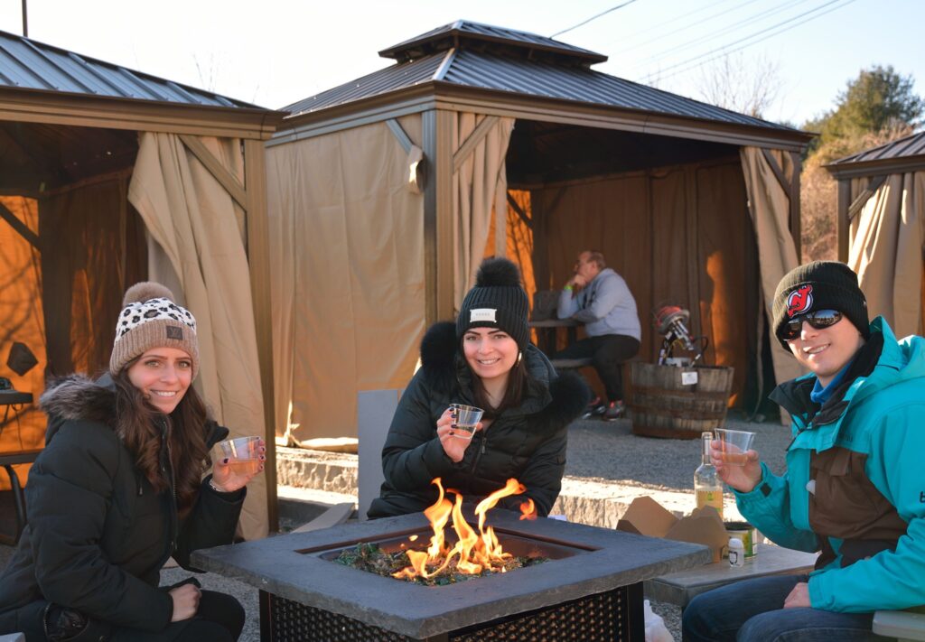 Guests sitting around a cozy fire pit at Old York Cellars, enjoying wine while surrounded by private cabanas on a cool day.