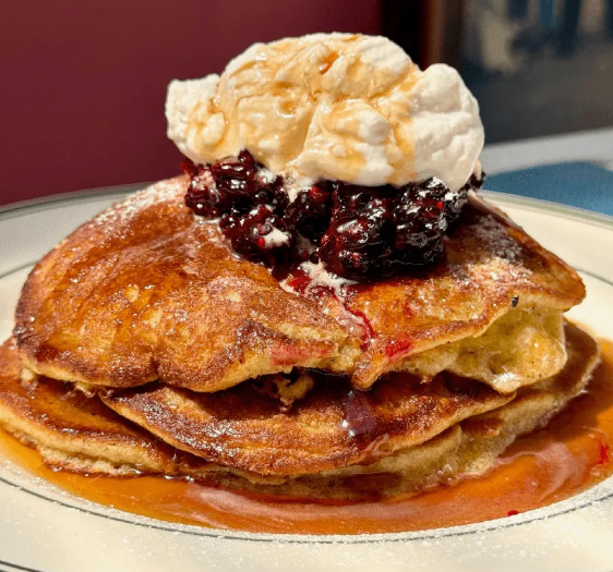 Stack of golden pancakes topped with whipped cream and berry compote at Uncle Rocco in Hoboken, NJ.