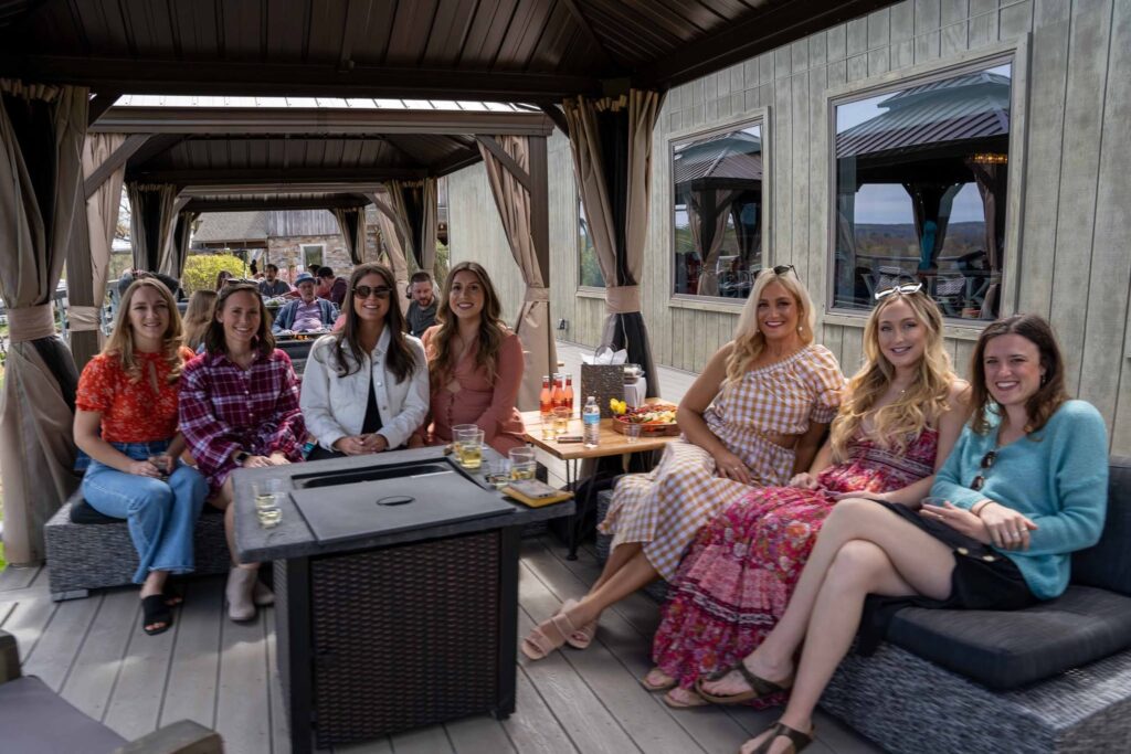 Group of guests enjoying brunch in a cozy cabana with cushioned seating and a fire table at Old York Cellars Winery in Ringoes, New Jersey.