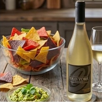 Colorful tortilla chips served with fresh guacamole and red salsa alongside a bottle and glass of Old York Cellars Sauvignon Blanc white wine for party snack pairings.