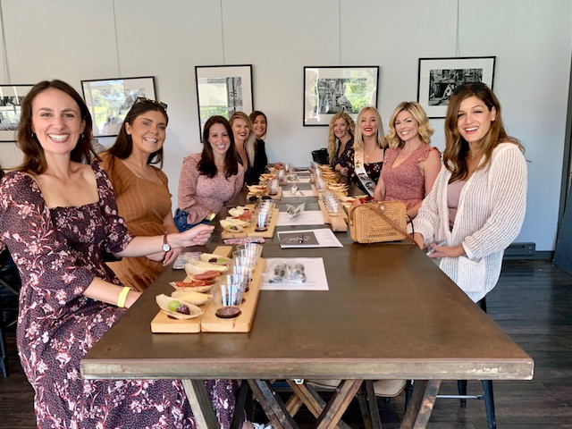 A group of friends seated around a long table at Old York Cellars in Ringoes, NJ for an indoor wine tasting. Wooden boards with cheeses, crackers, and wine flights create a lively Central NJ wine and food pairing atmosphere.