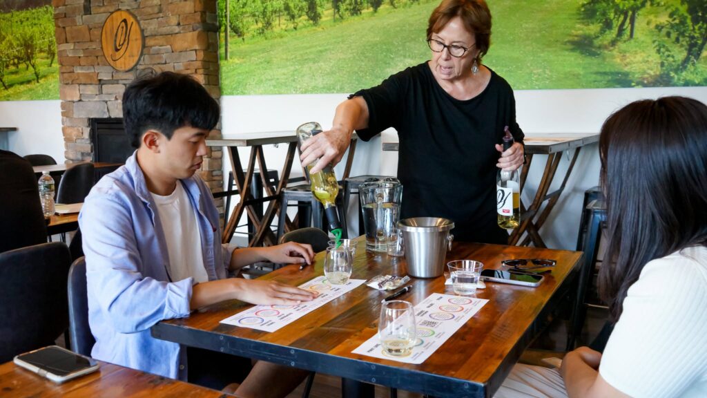 Old York Cellars staff member pours white wine for guests during a guided tasting in Ringoes, NJ. Wooden tables, tasting mats, and vineyard décor create a relaxed Central NJ wine tasting experience.