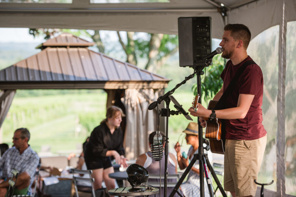 Musician performing live acoustic set at Old York Cellars Winery in Ringoes, NJ, with guests relaxing and enjoying wine under the cabana.