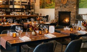 Elegant dining room at Old York Cellars in Ringoes, NJ set for a seasonal wine pairing dinner. Wooden tables are decorated with autumn centerpieces, amber candles, and neatly arranged wine glasses beside a glowing stone fireplace, creating a warm and inviting Central NJ winery atmosphere.