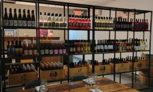 Old York Cellars Wine & Gift Shop in Hunterdon County NJ. Wall of neatly arranged wine bottles and branded wooden crates in a winery tasting room, with glasses set on a table in the foreground.