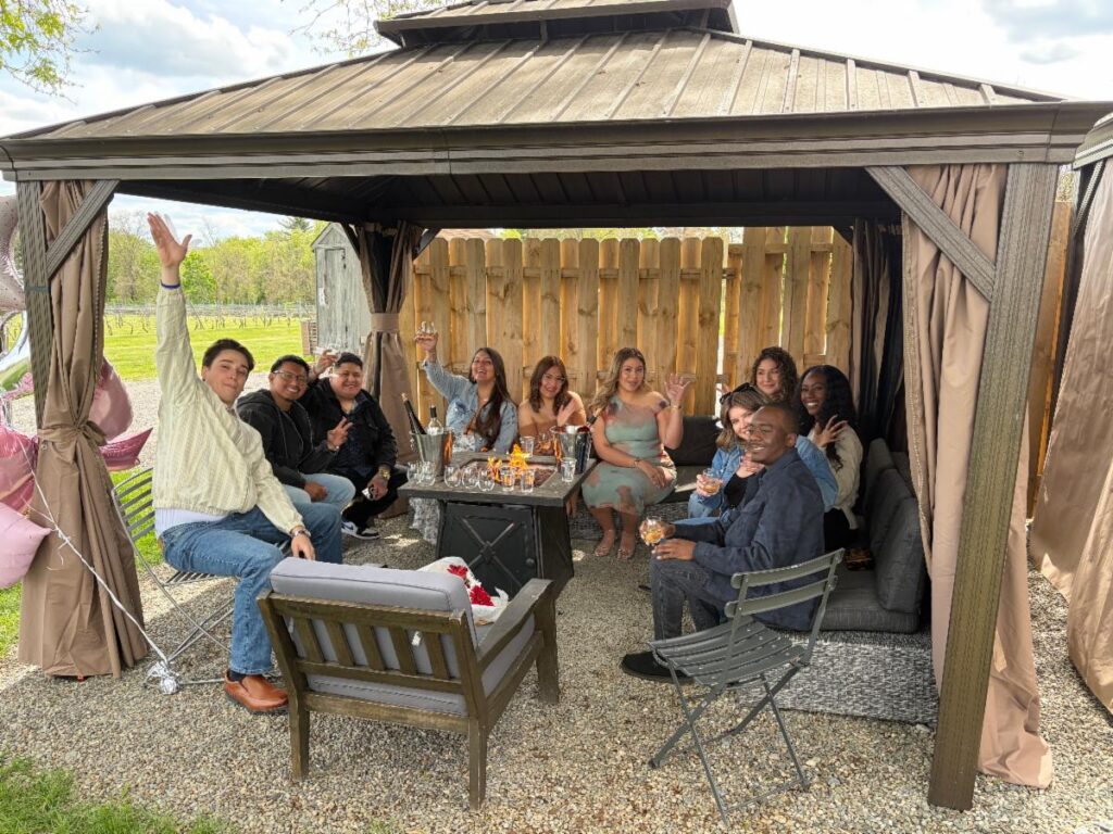 Guests gather under a private cabana at Old York Cellars in Ringoes, NJ for a relaxed outdoor wine tasting. The group enjoys wine and snacks in a rustic setting surrounded by wooden fencing and gravel paths.