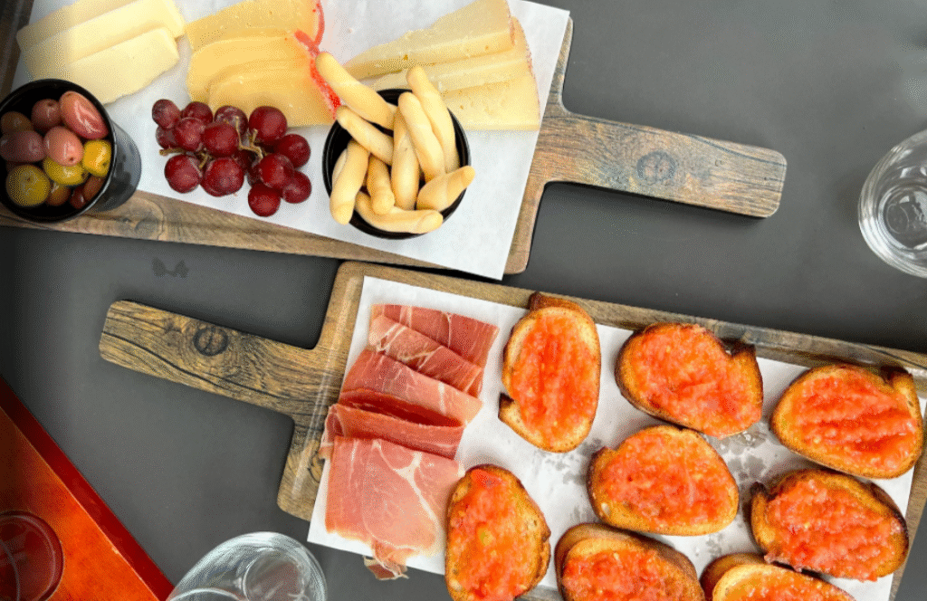 Two wooden boards at Old York Cellars in Ringoes, NJ displaying sliced cheeses, prosciutto, olives, grapes, breadsticks, and tomato‑topped crostini. A colorful spread showcasing Central NJ wine tasting and culinary pairings.