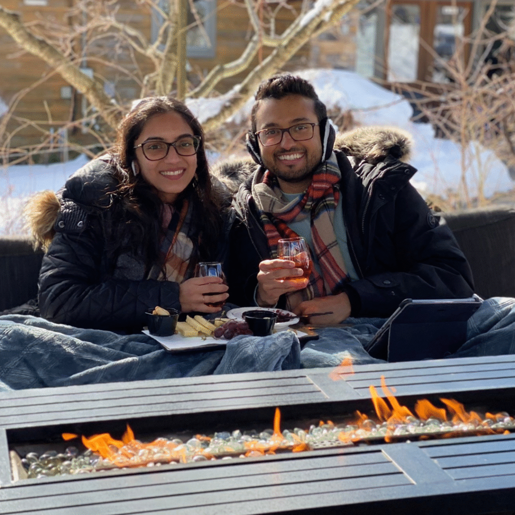 Couple seated by a fire table holding drinks, bundled up for a cool outdoor brunch at Old York Cellars Vineyard in Hunterdon County, NJ.