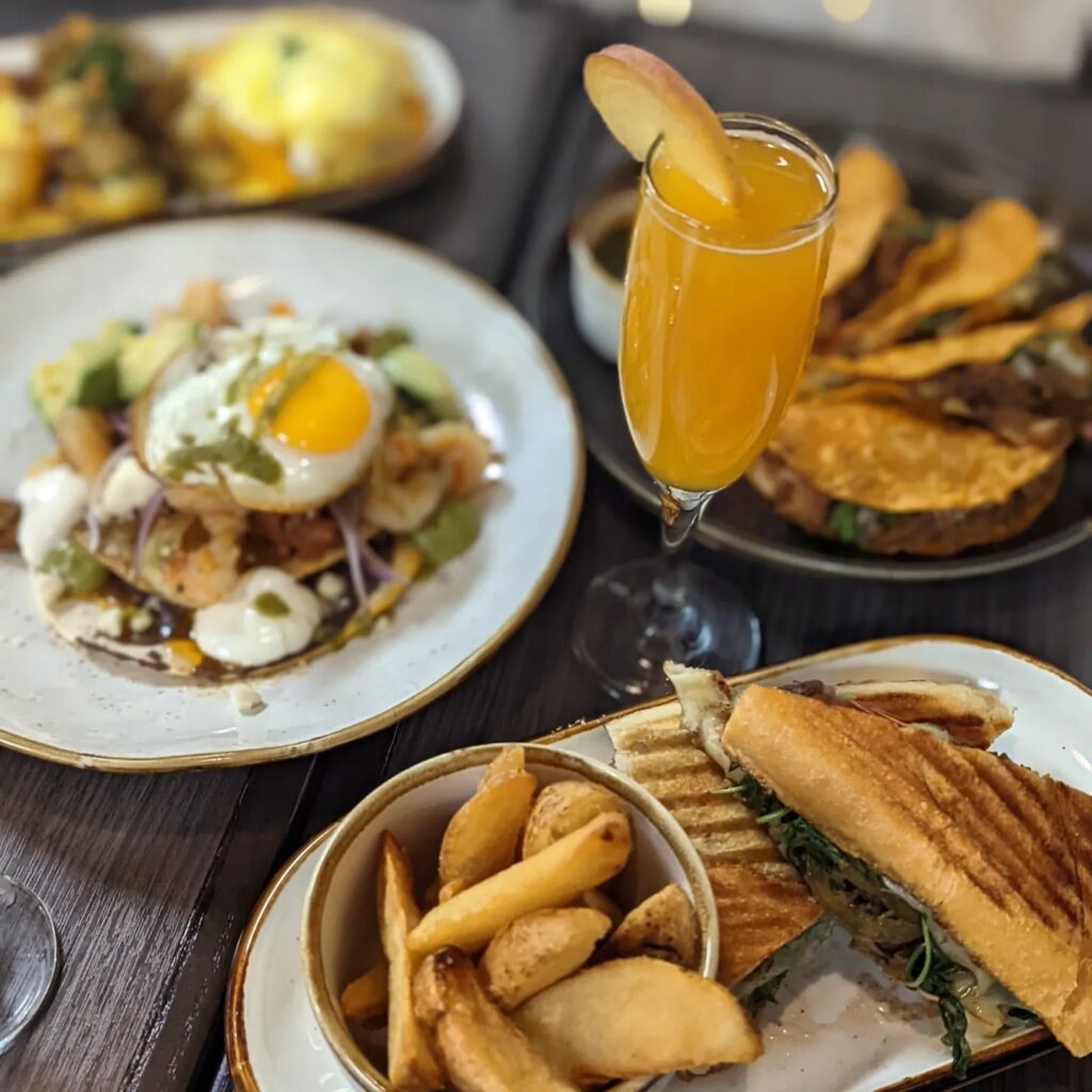 Table spread at Brunch by De Martino in Somerville, NJ, featuring avocado toast, sandwiches, and a mimosa.
