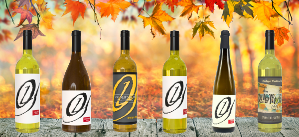 Six bottles of Old York Cellars white wines displayed on a wooden surface with fall leaves and golden forest background.